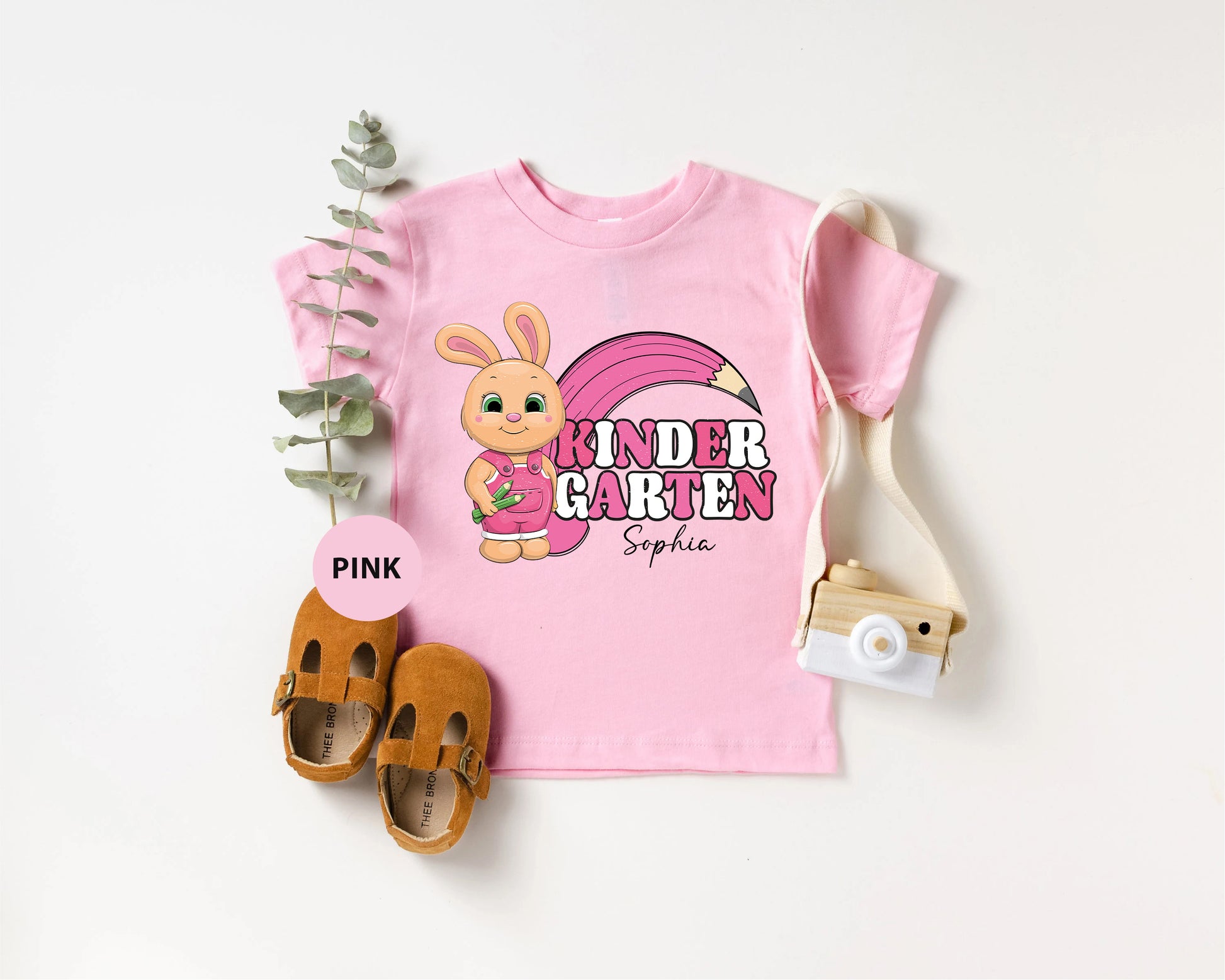 a pink shirt with a pink bunny on it next to a pair of baby shoes
