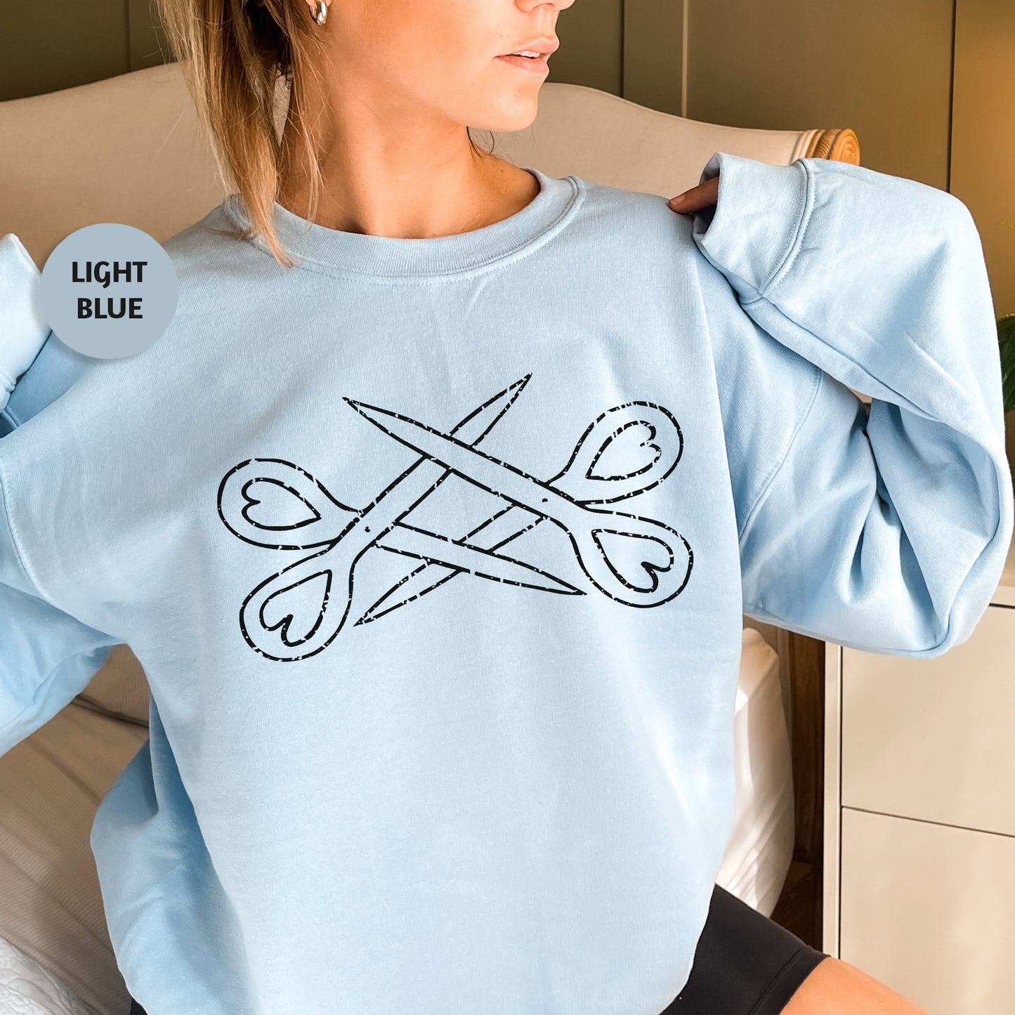 a woman sitting on a bed wearing a light blue sweatshirt