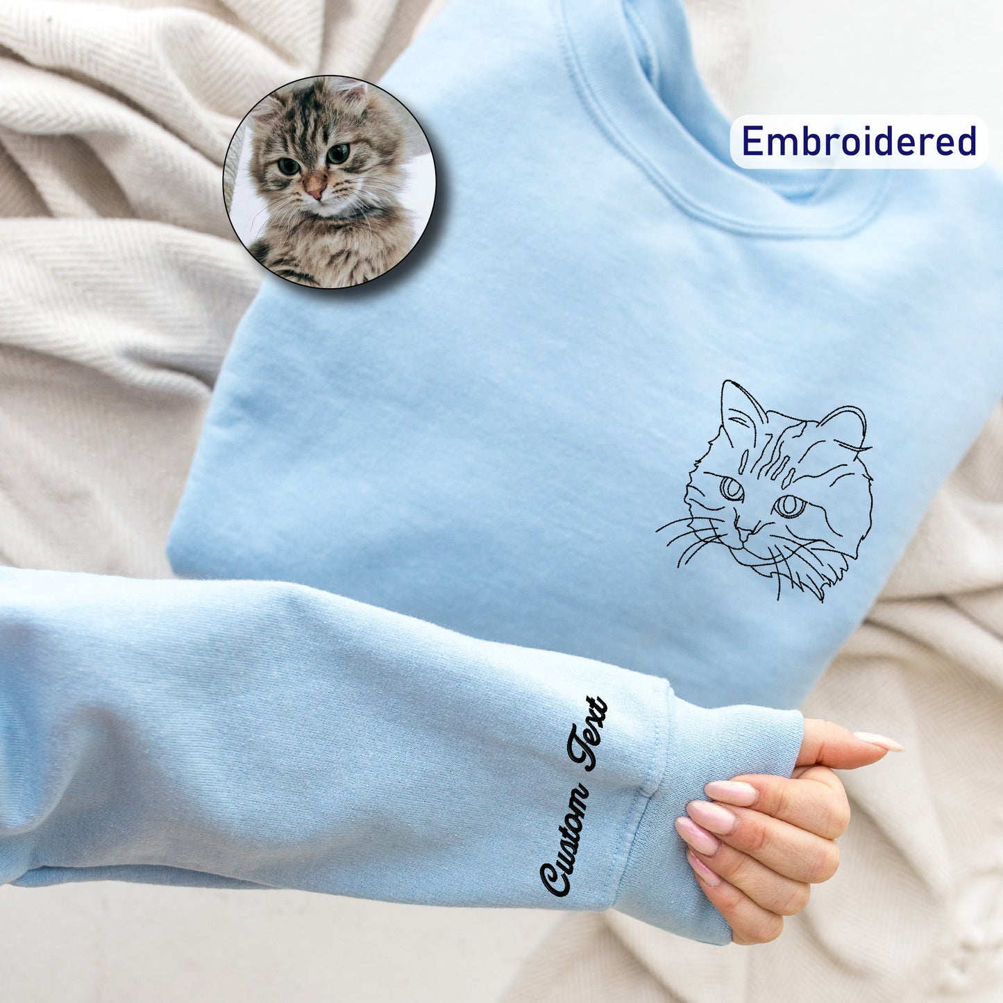 a person's hand holding a blue sweater with a cat drawn on it