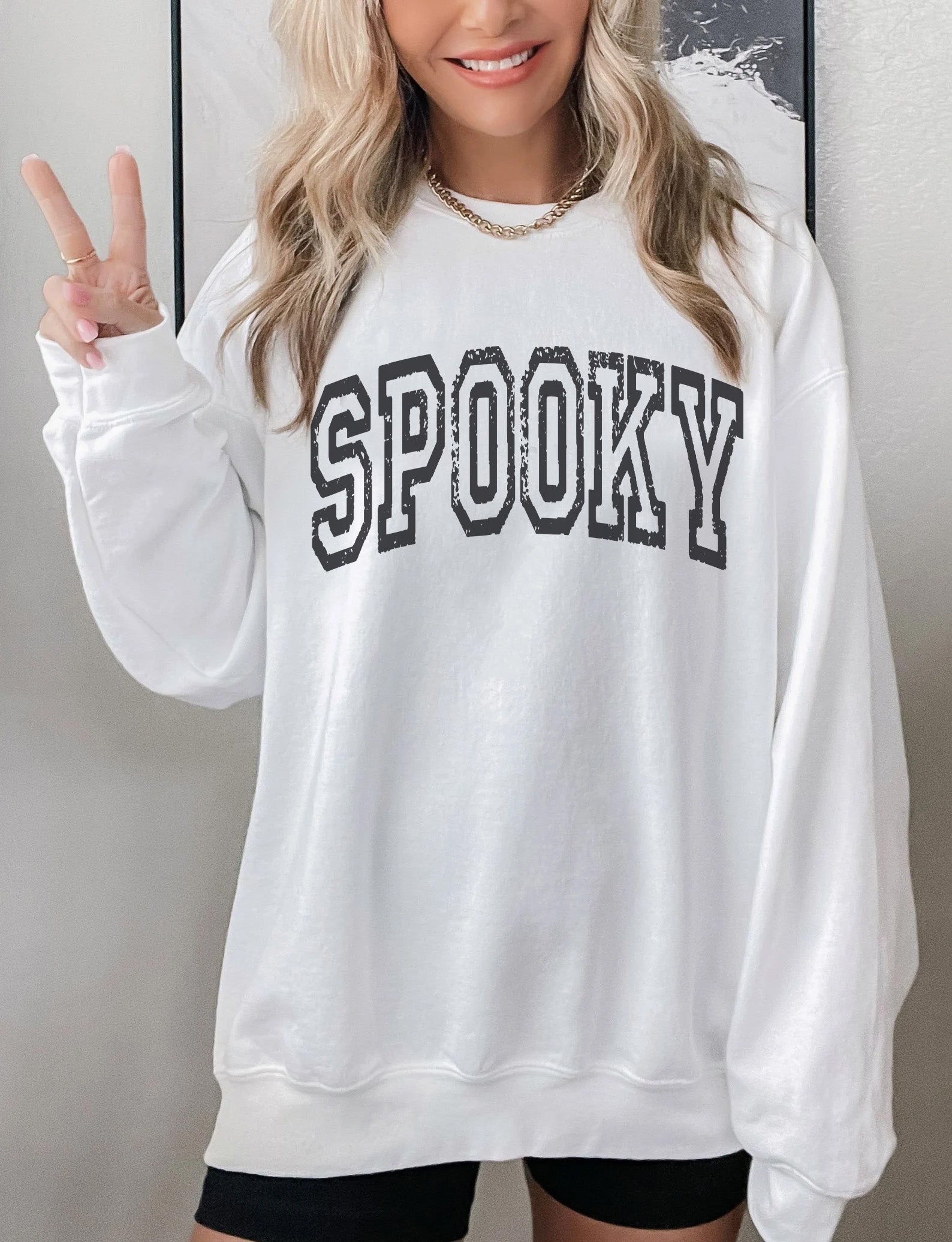 a woman wearing a white sweatshirt with the word spooky on it