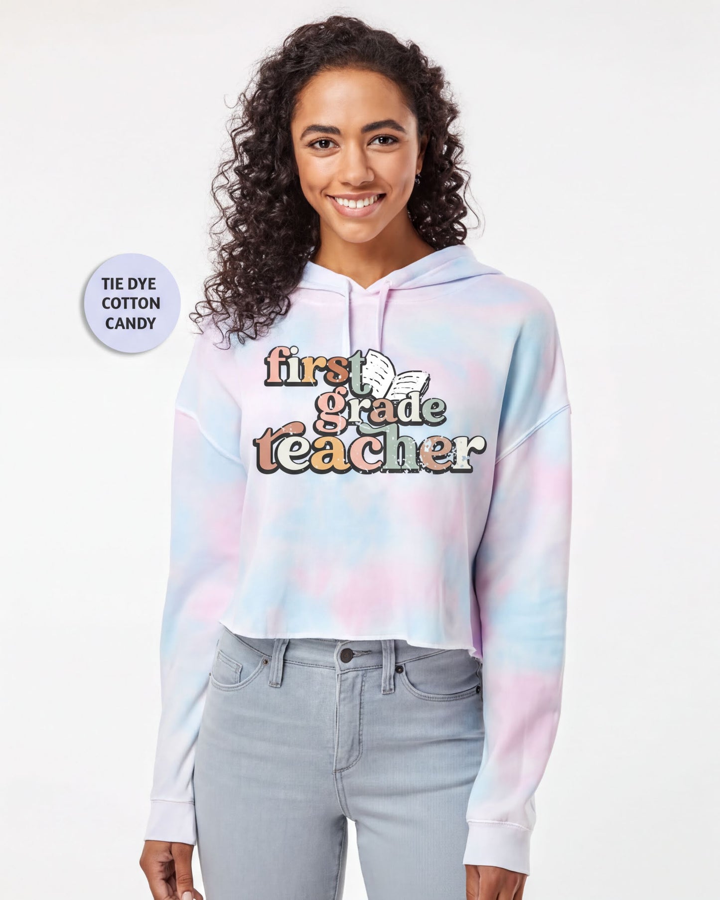 A smiling young woman wearing a tie-dye hoodie with the text "first grade teacher" printed on it.