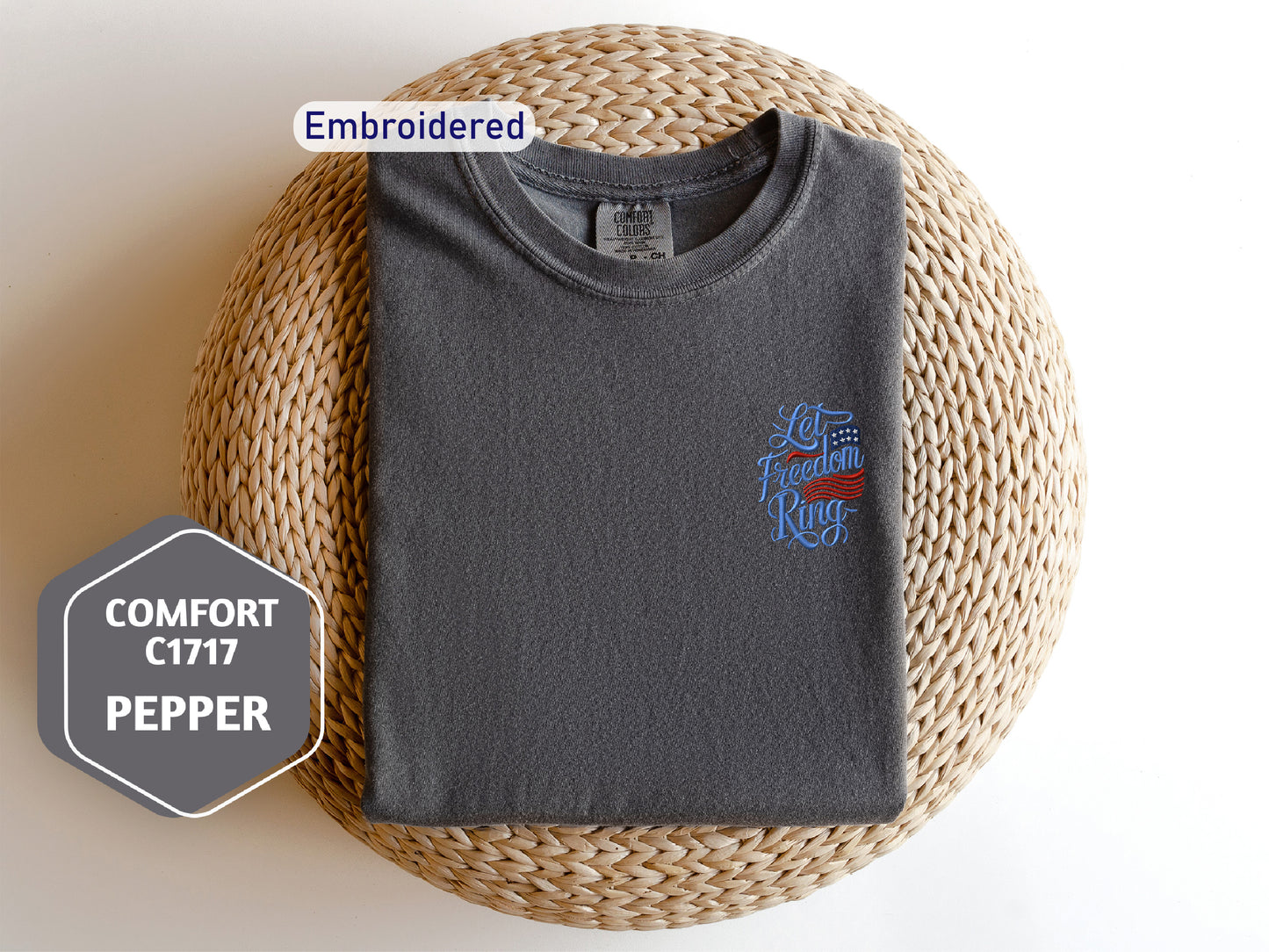 a gray t-shirt with a blue and red design on the front, laid out on a woven mat.