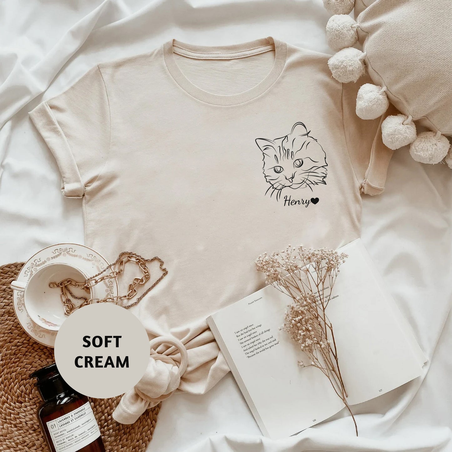 a white t - shirt with a cat on it next to a bottle of cream