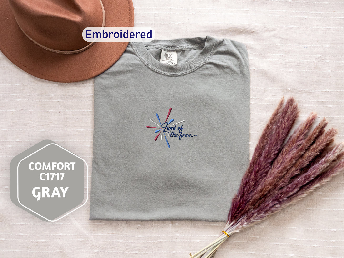 a gray t-shirt with a patriotic design, a brown hat, and a bunch of purple and red pom poms, all arranged on a white background.