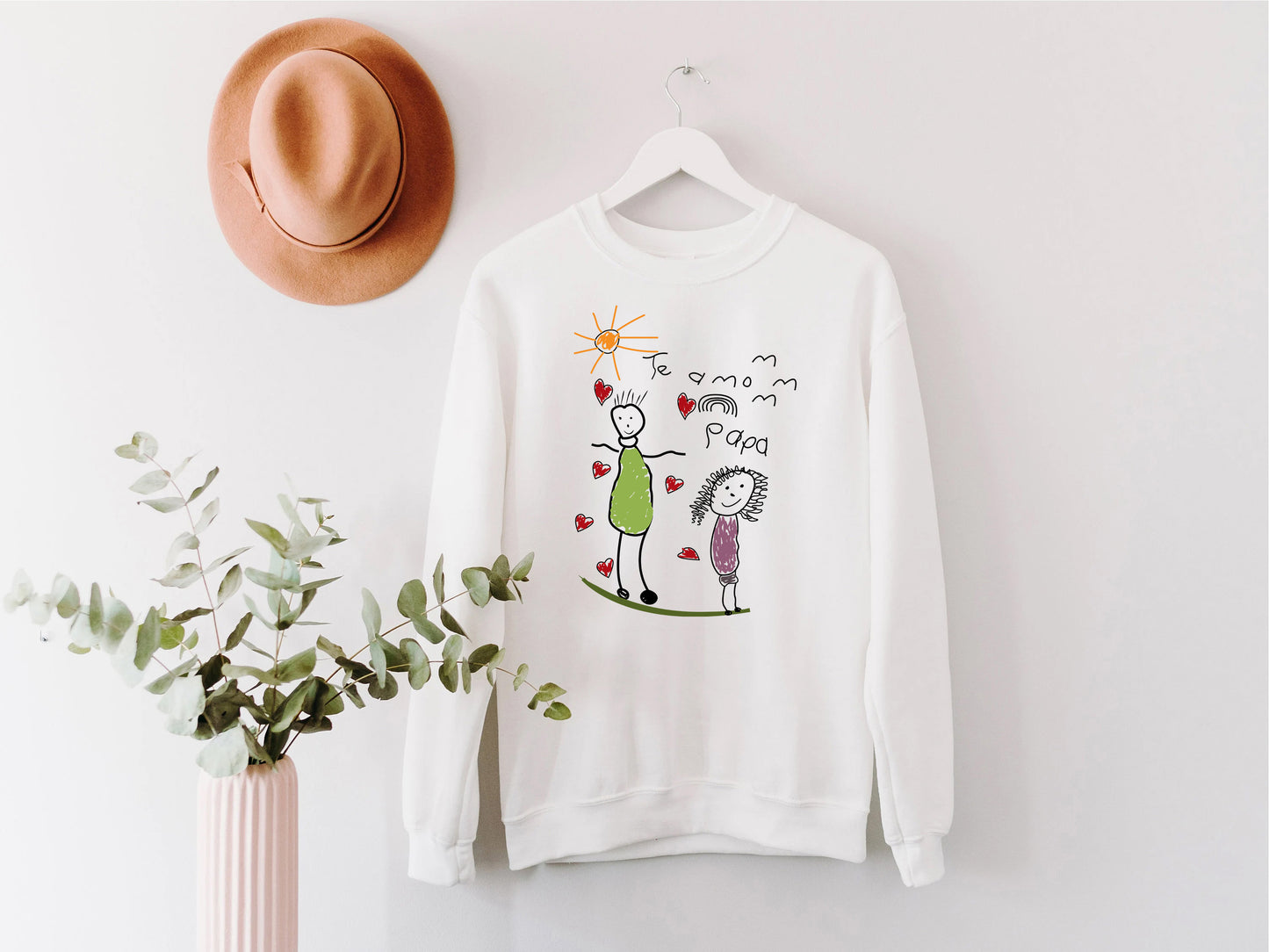 a white sweater hanging on a wall next to a plant