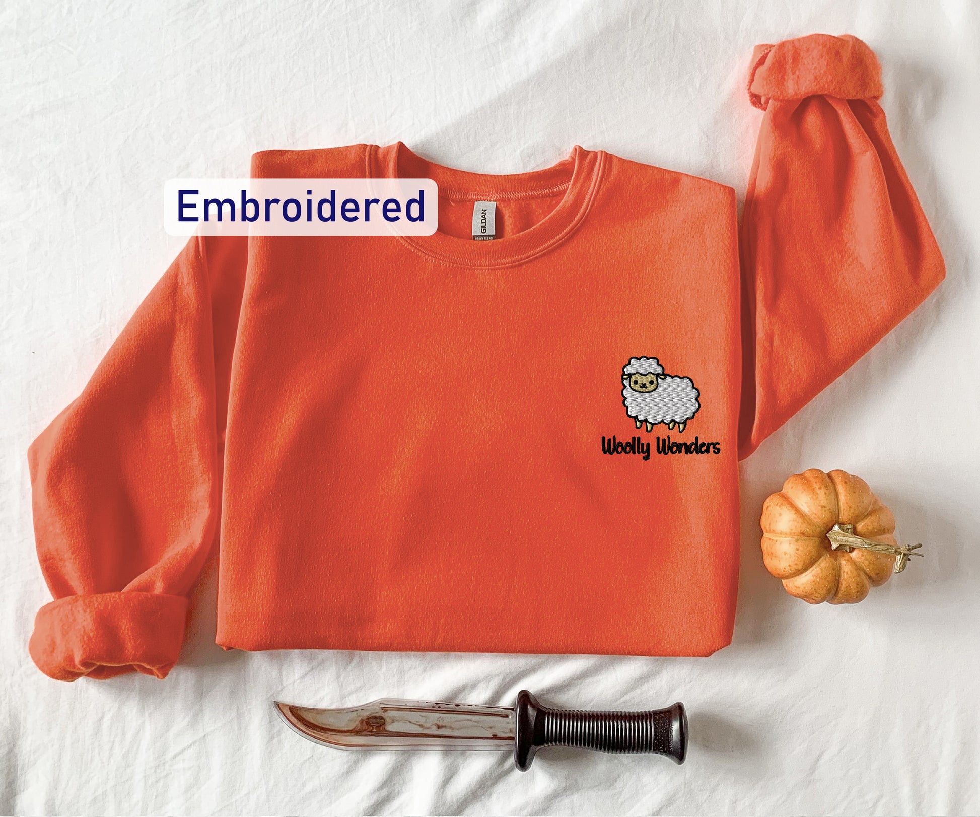 an orange shirt with a sheep embroidered on it next to a knife