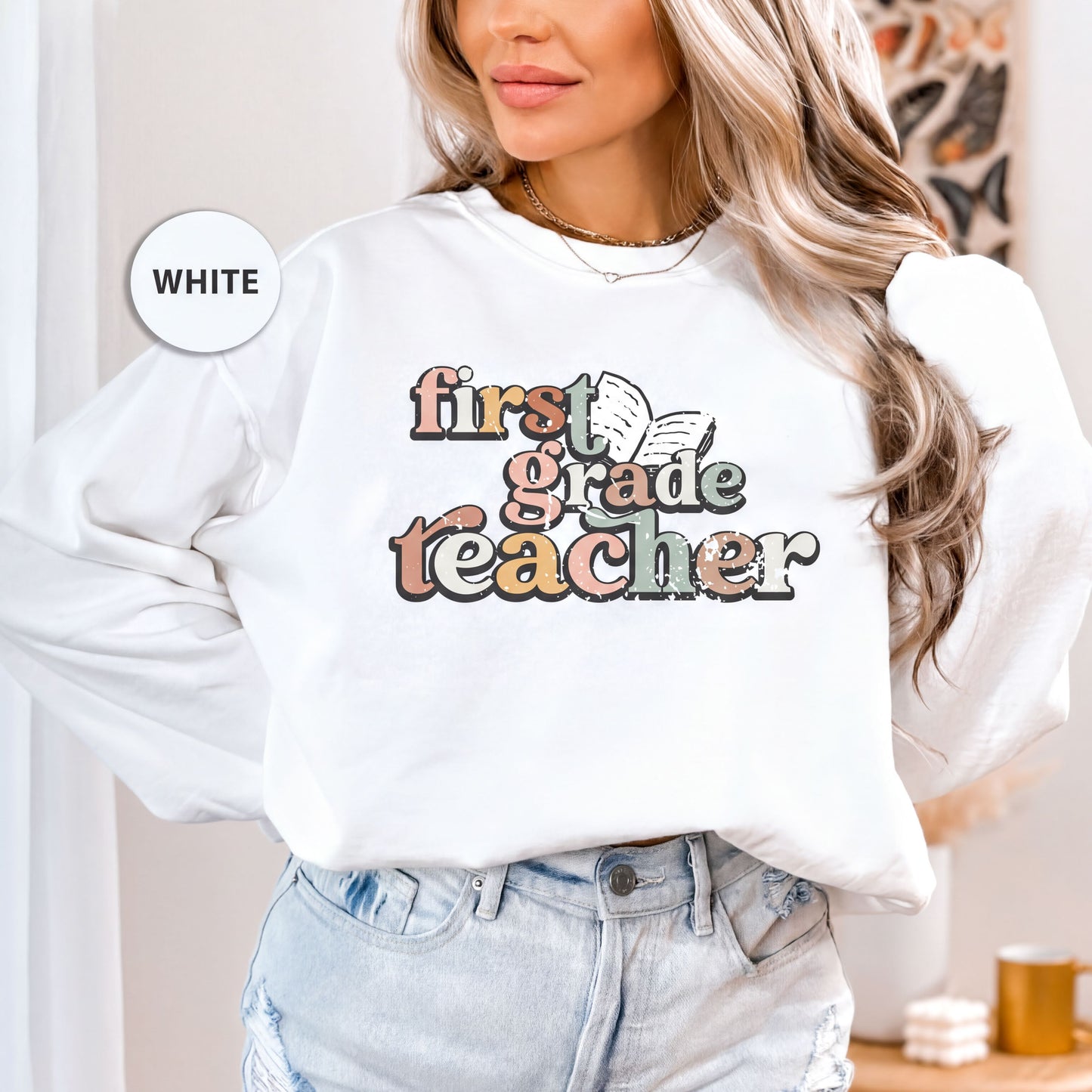 A woman wearing a white long-sleeved shirt with a colorful graphic design that says "first-grade teacher" printed on it.