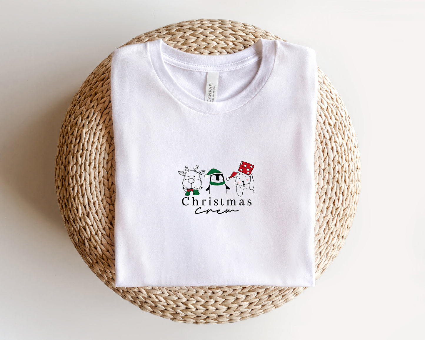 A white t-shirt with a Christmas-themed graphic design printed on it, placed on a woven basket.