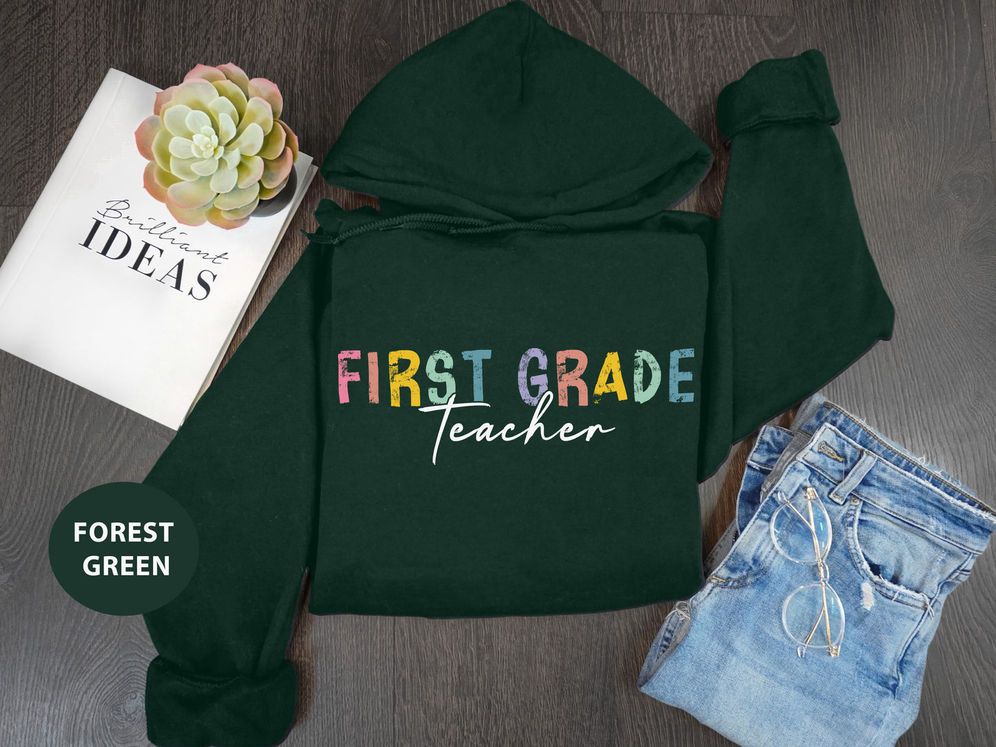 a green hoodie with the words first grade teacher next to it