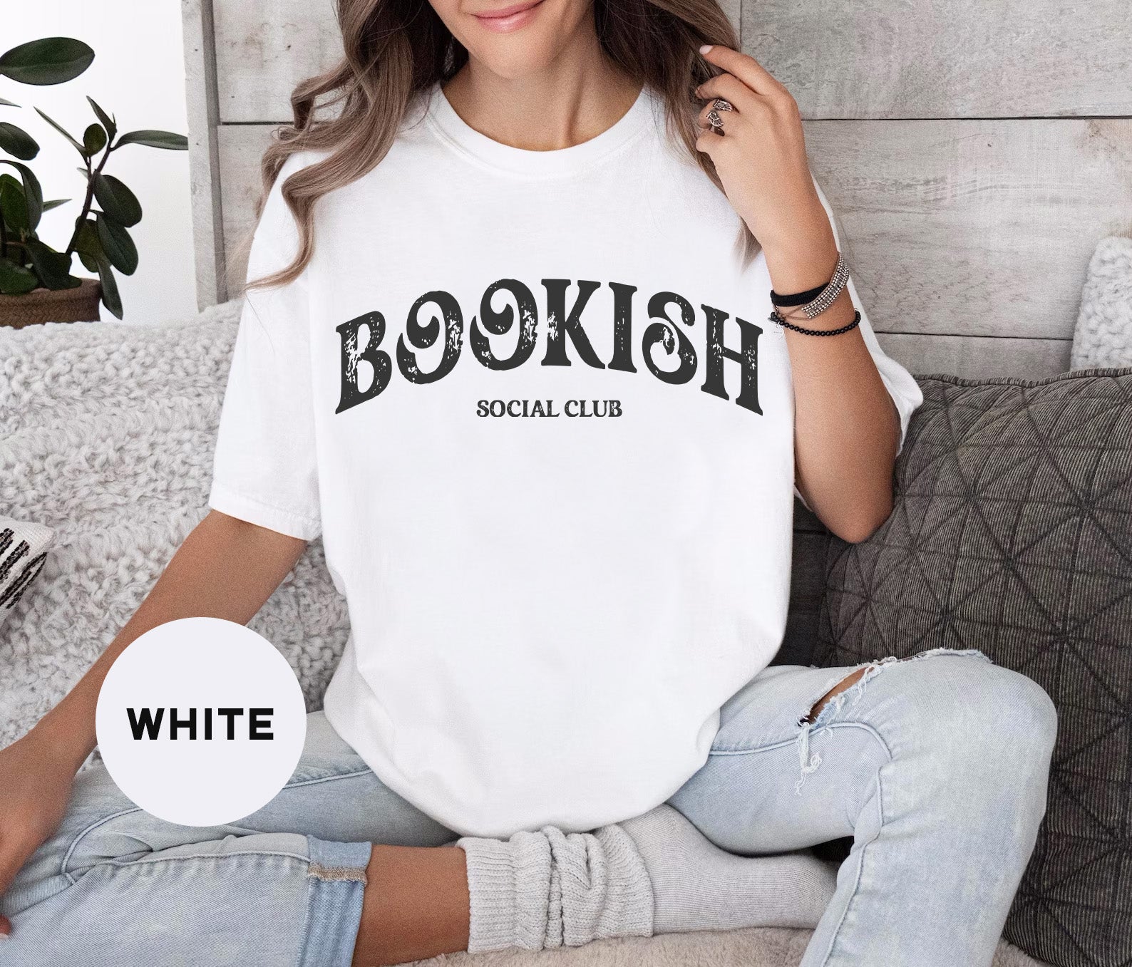 a woman sitting on a couch wearing a bookish social club shirt