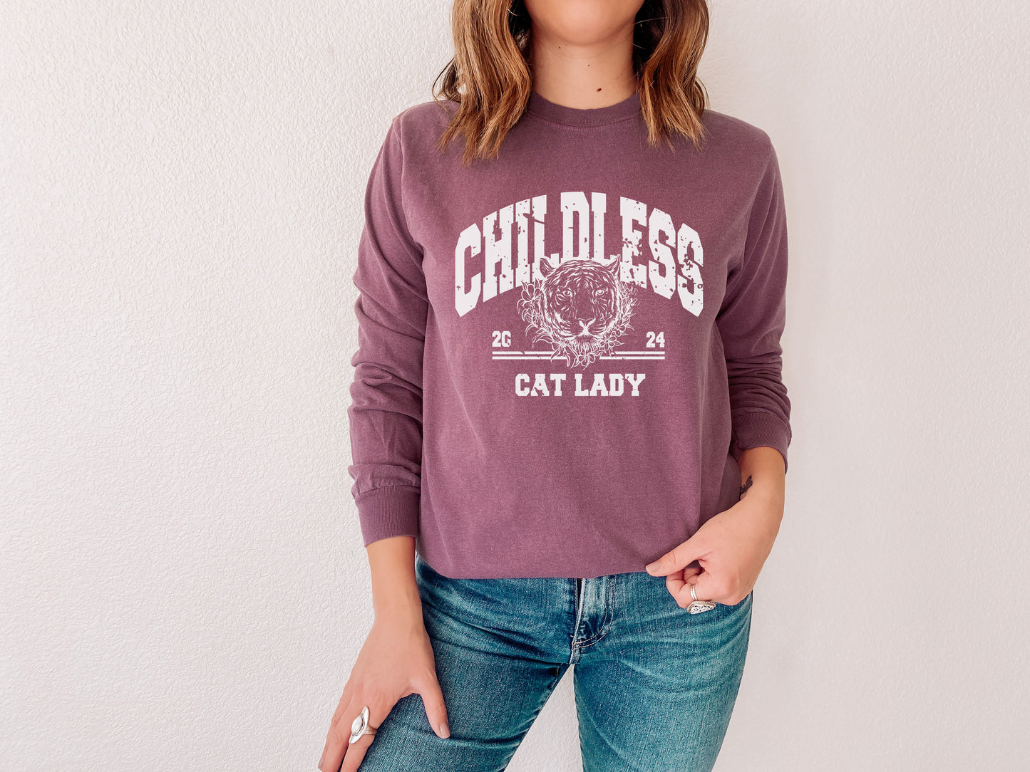 a woman wearing a cat lady sweatshirt standing in front of a white wall