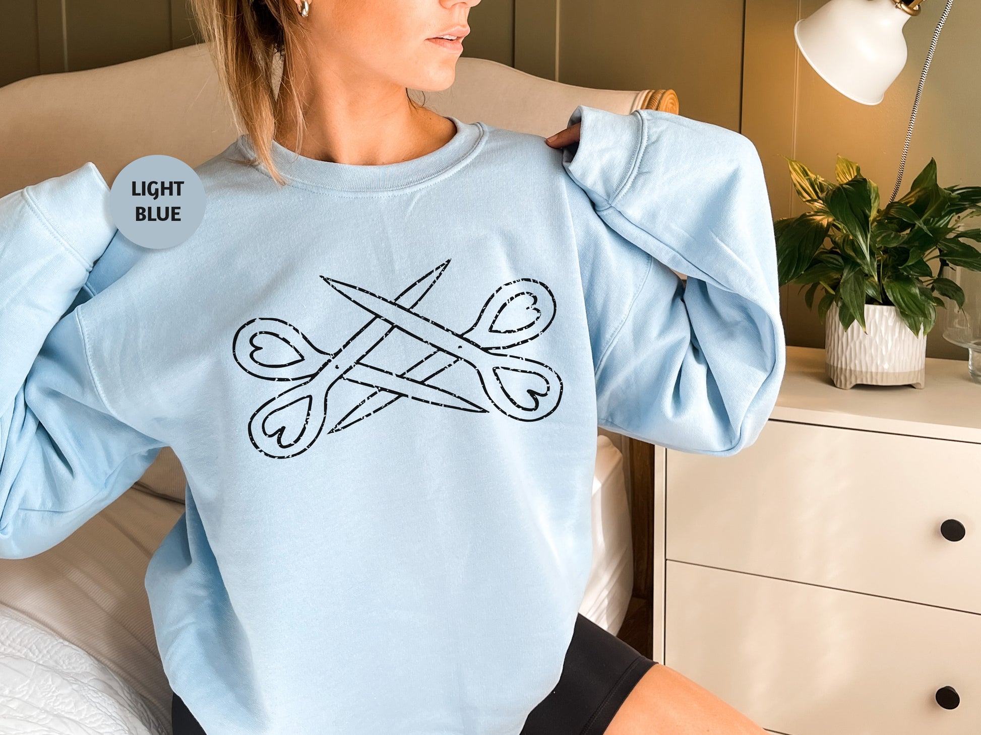 a woman sitting on a bed wearing a light blue sweatshirt