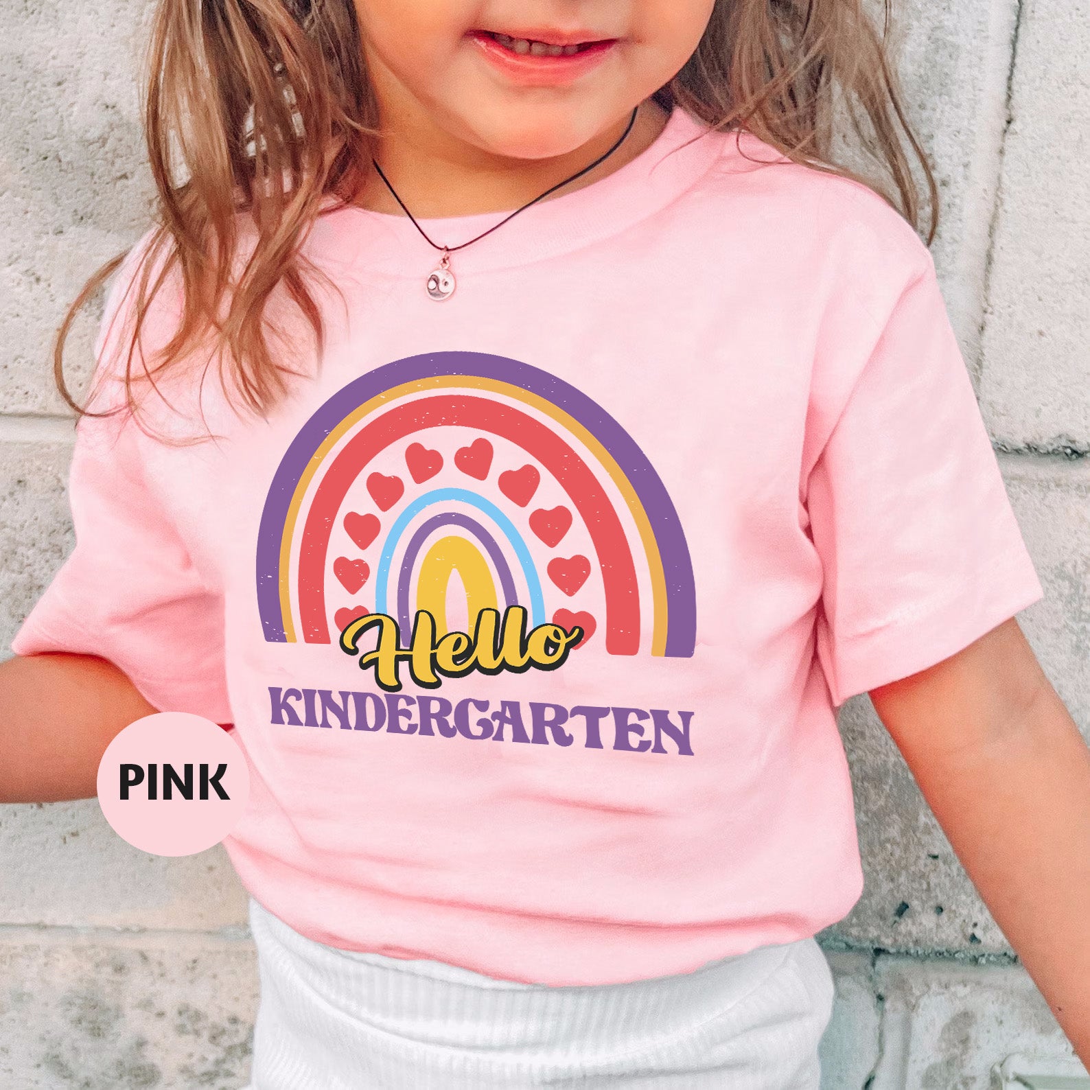 a little girl wearing a pink shirt with a rainbow on it