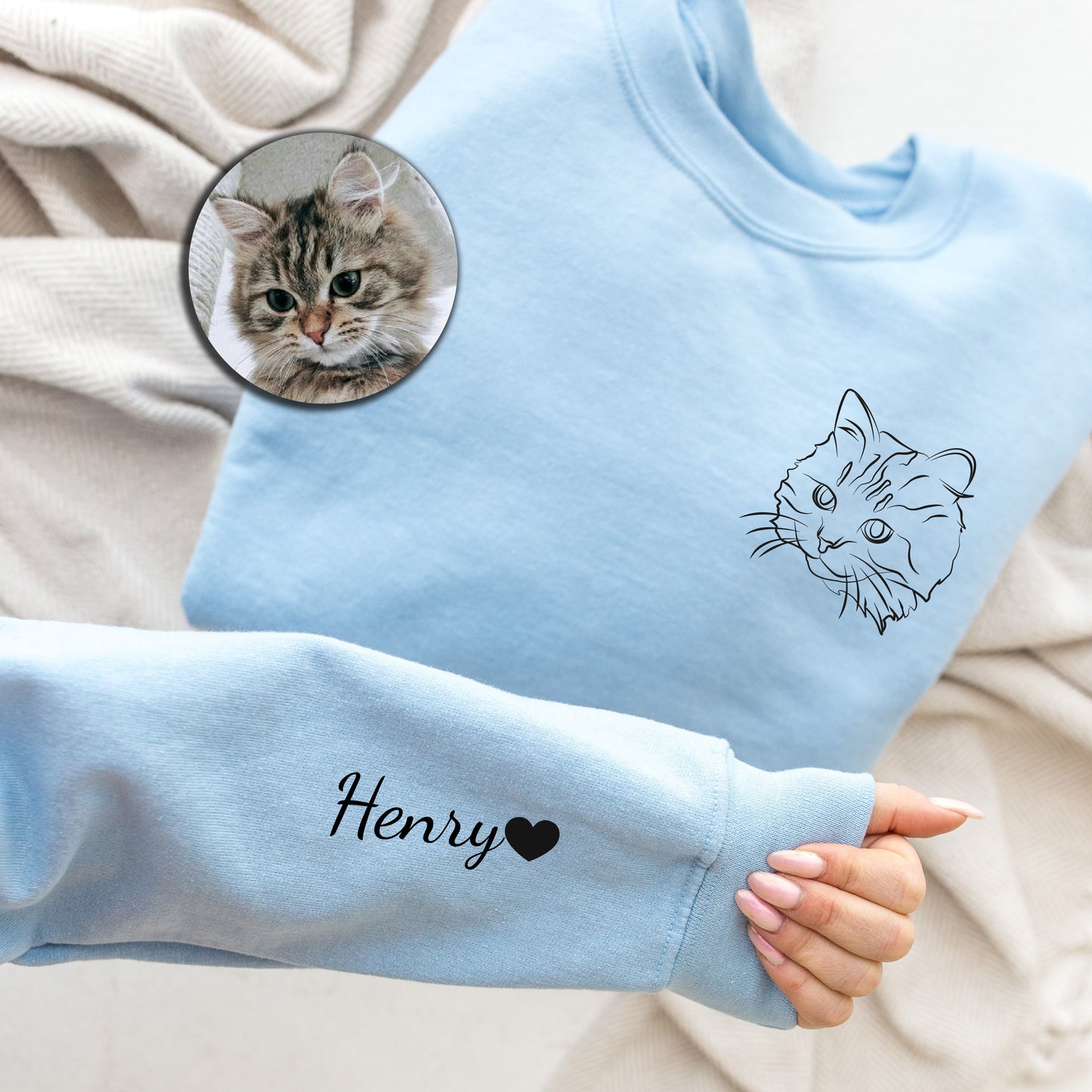 a person's hand holding a blue sweater with a picture of a cat on