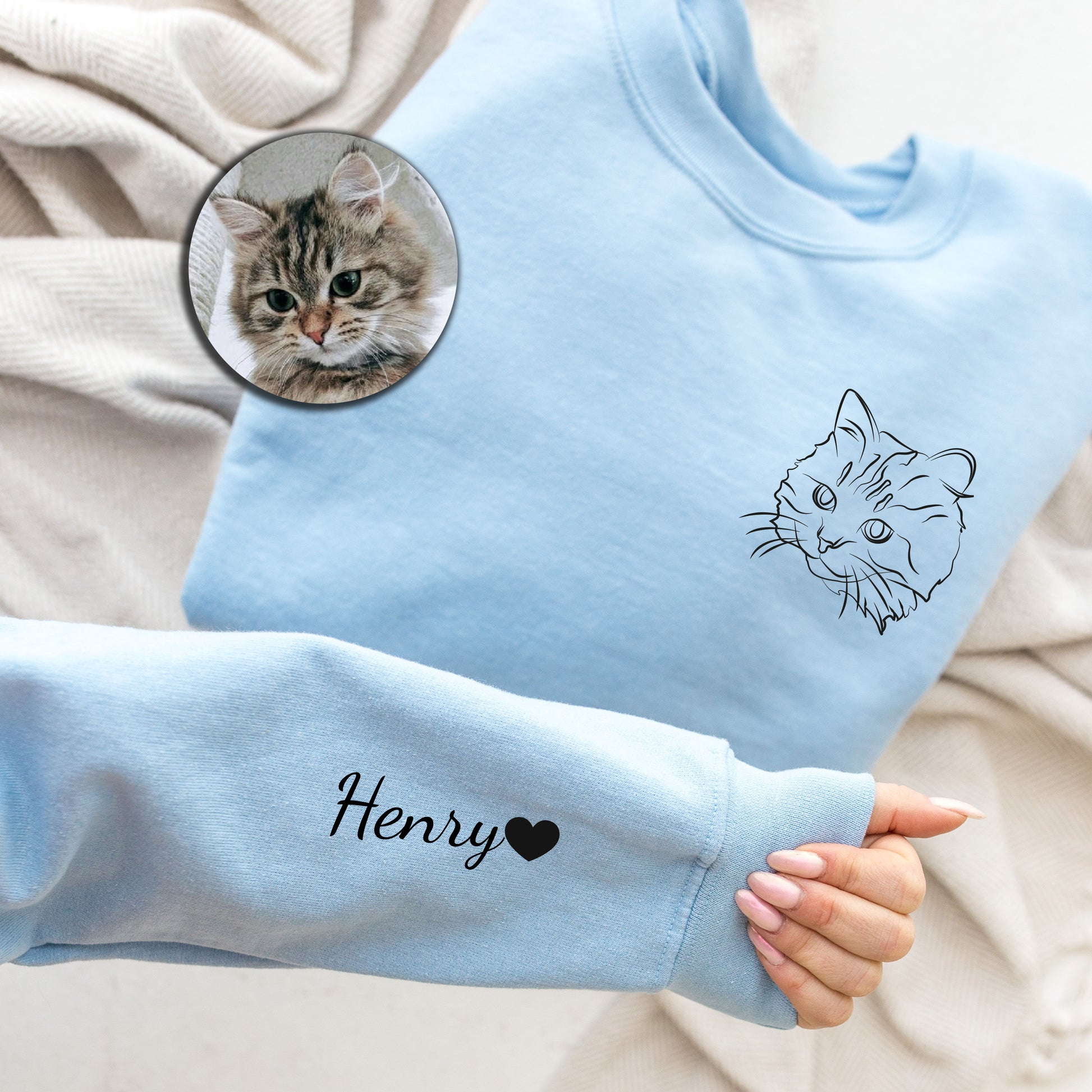 a person's hand holding a blue sweater with a picture of a cat on