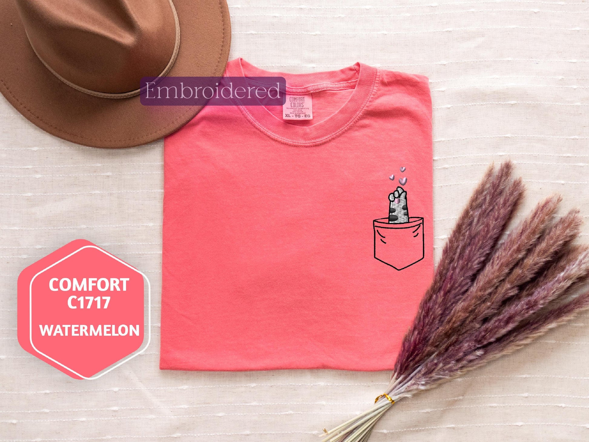 a pink shirt with a picture of a cat in a pocket and a straw hat