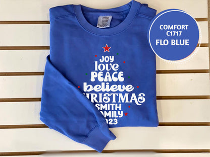 A blue long-sleeved shirt with white text and a Christmas tree design, placed on a white surface.
