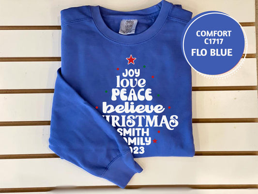 A blue long-sleeved shirt with white text and a Christmas tree design, placed on a white surface.