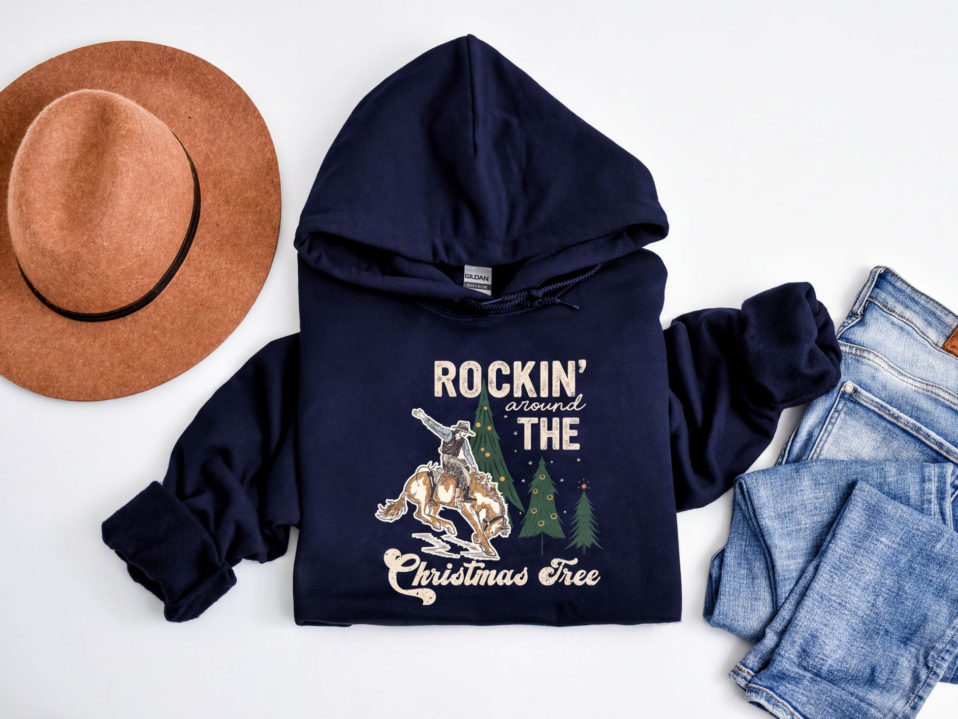 A navy blue hoodie with a graphic design, a brown fedora, a pair of jeans, and a Christmas tree on a white background.
