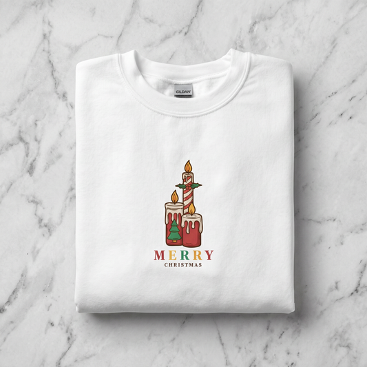 A white t-shirt with a graphic design of two lit candles and the text "MERRY CHRISTMAS" printed on it.