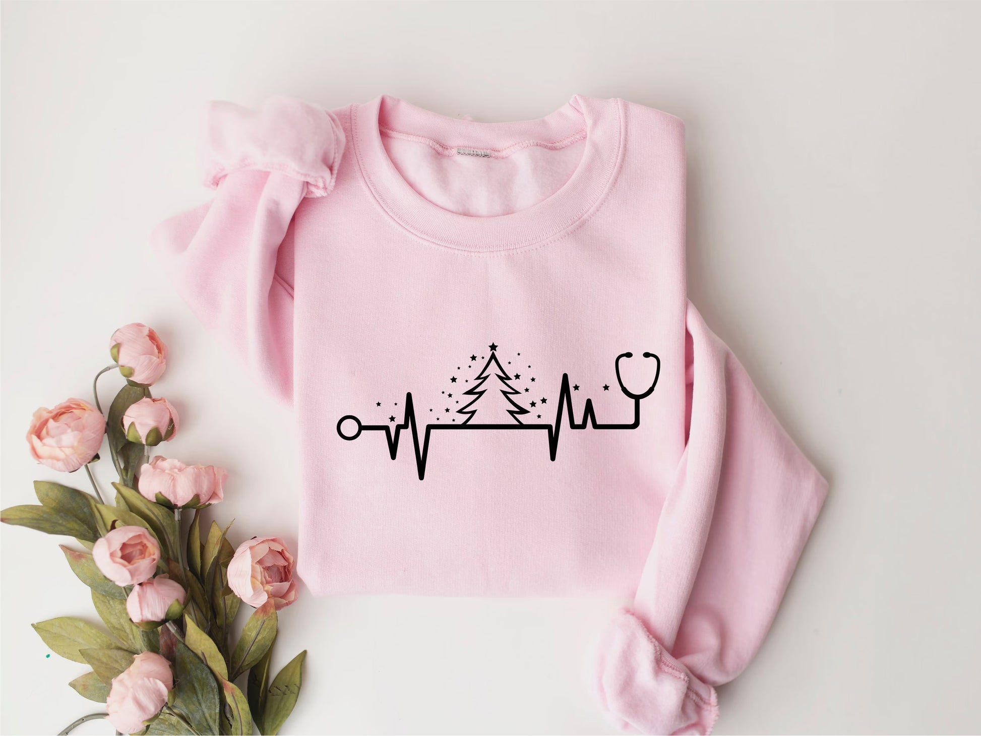 A pink sweatshirt with a black line graphic and a stethoscope symbol printed on it, along with a bouquet of pink flowers.