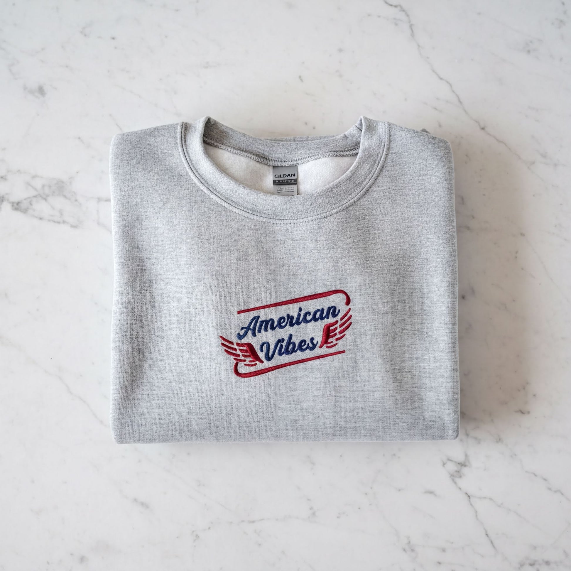 A gray sweatshirt with the text "American Vibes" printed on it, laid out on a marble surface.