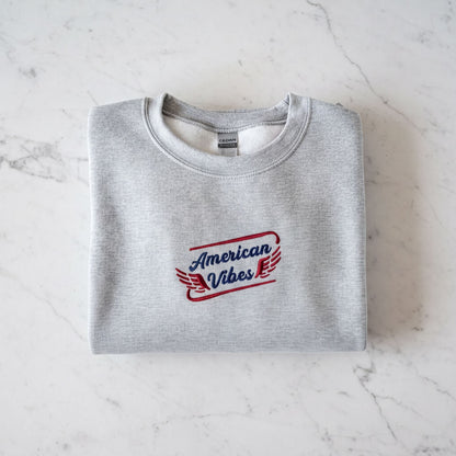 A gray sweatshirt with the text "American Vibes" printed on it, laid out on a marble surface.
