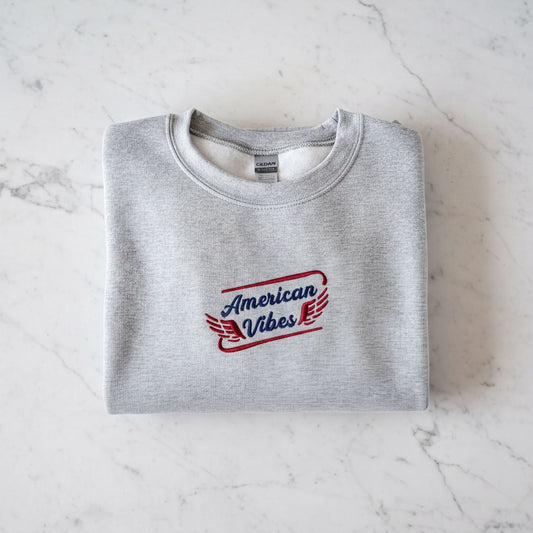 A gray sweatshirt with the text "American Vibes" printed on it, laid out on a marble surface.