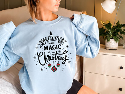A woman wearing a light blue sweater with a printed design that says "Believe in the Magic of Christmas".