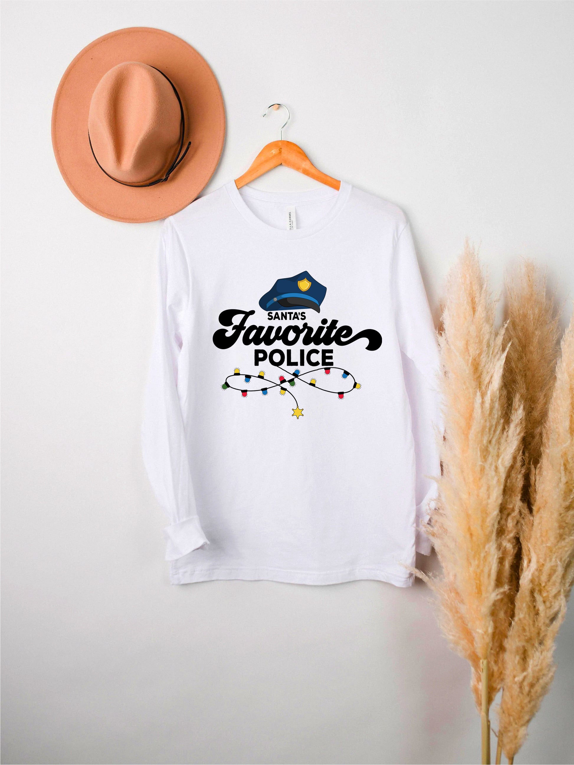 A white long-sleeved t-shirt with a graphic design and text, hanging on a wooden hanger. The text on the t-shirt says "Police favorite".