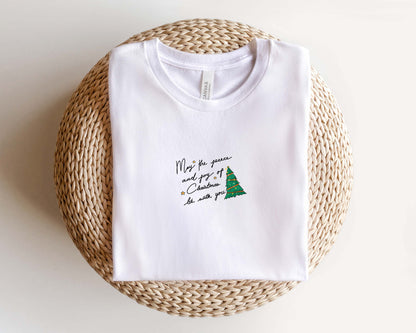 A white t-shirt with a Christmas tree design and text printed on it, placed on a woven basket.