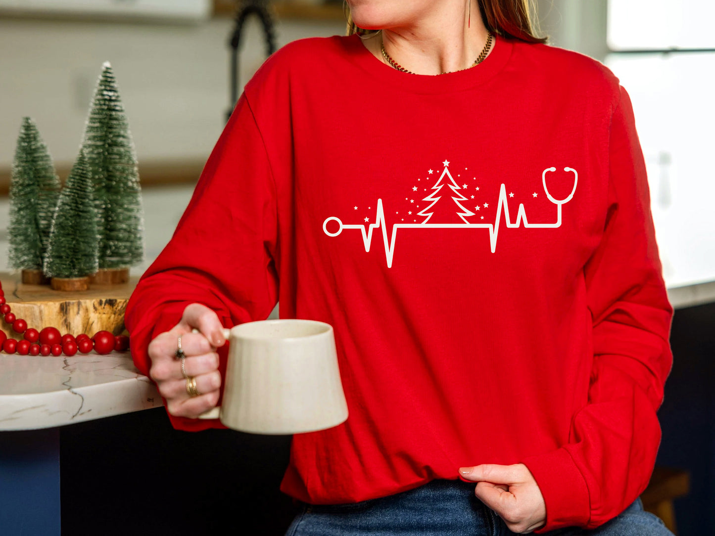 A person wearing a red sweater with a white line design and a stethoscope on it is holding a coffee mug.