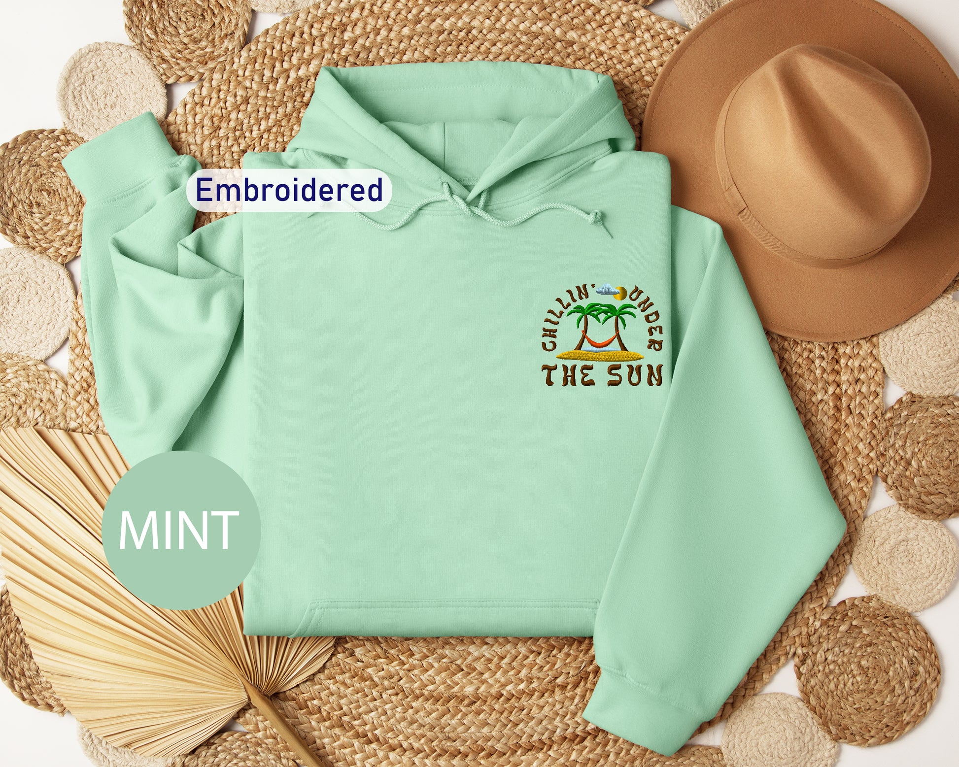a mint green hoodie with a tropical beach-themed design, including palm trees and the phrase "Chillin' under the sun". The hoodie is embroidered with the text "Embroidered" and "MINT" is written in a circular shape at the bottom left corner.