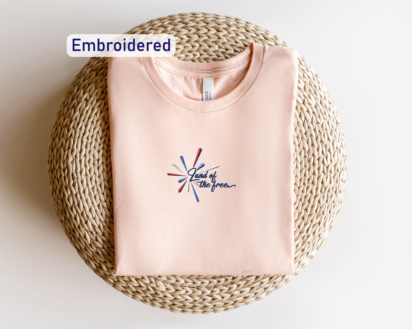 a pink t-shirt with a colorful embroidered design, laid out on a woven mat or placemat.