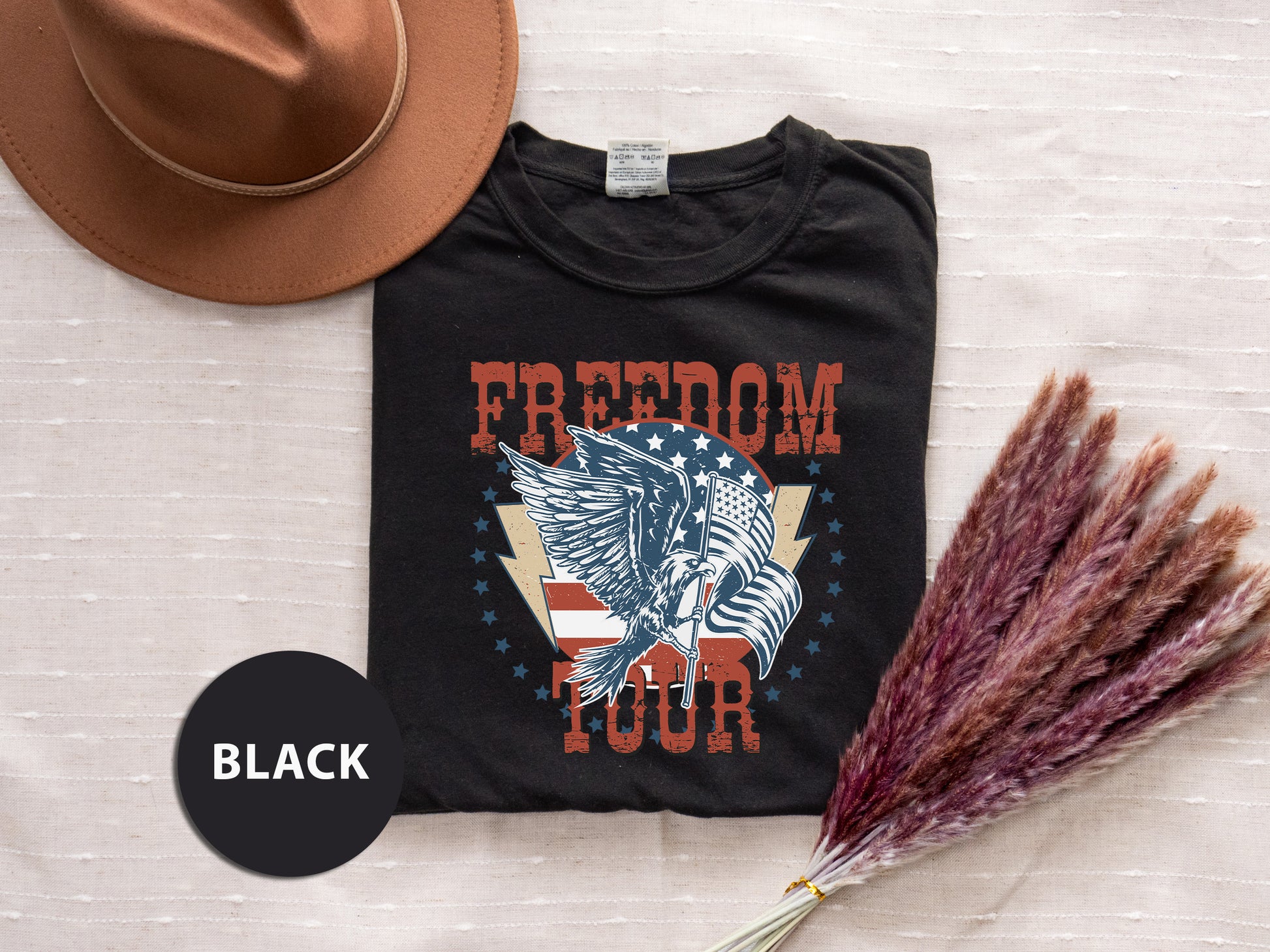a black t-shirt with a graphic design, a brown hat, and some purple flowers, all laid out on a surface.