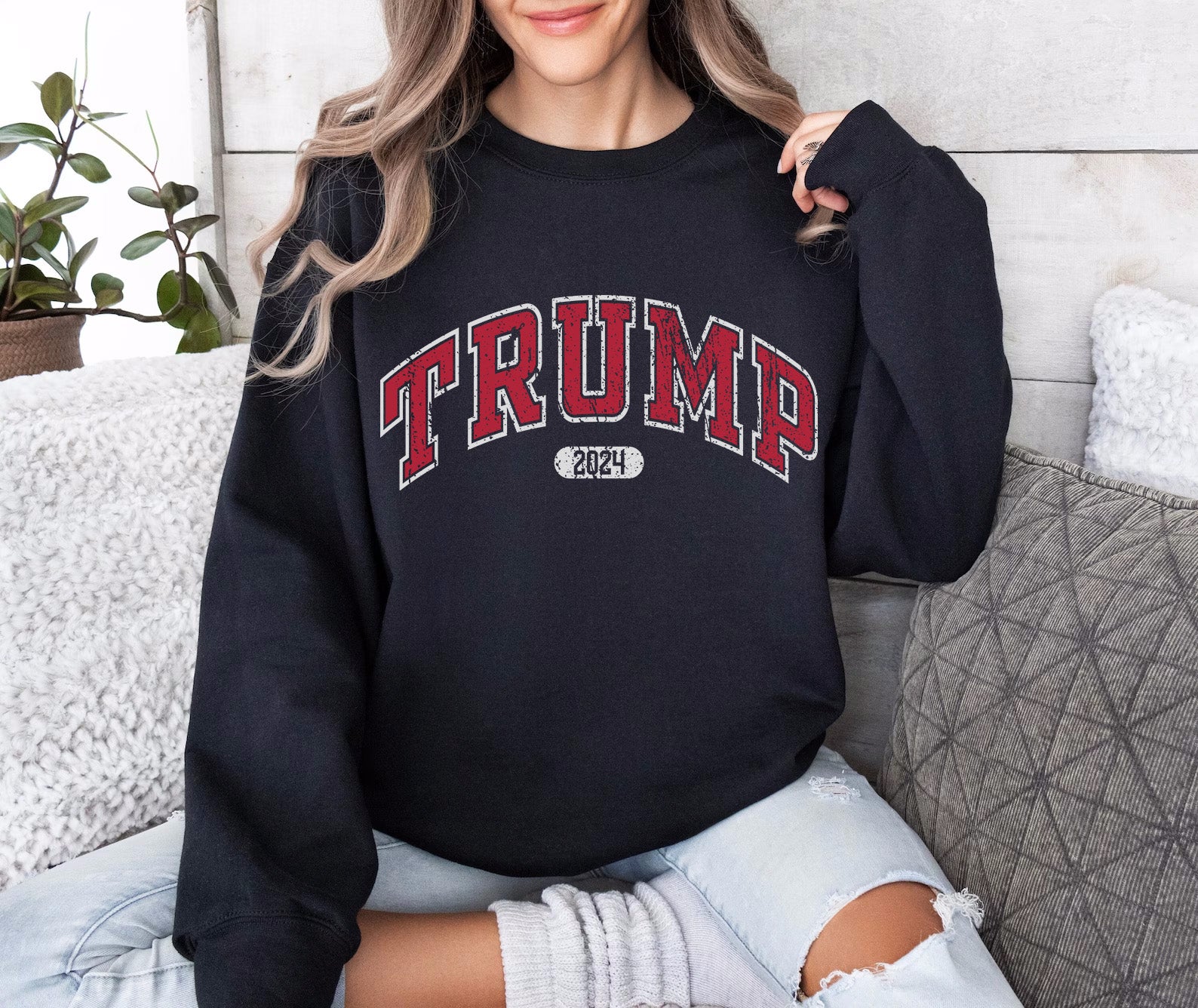 a woman sitting on a couch wearing a black trump sweatshirt