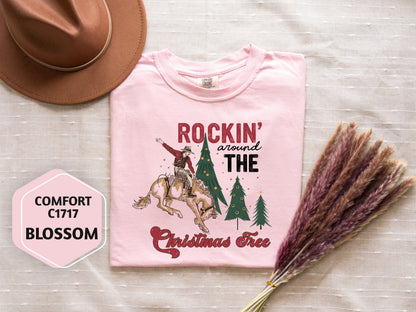 a pink t-shirt with a cowboy riding a bucking bronco, a cowboy hat, a pink flower, and a bunch of purple reeds, all arranged on a white background.