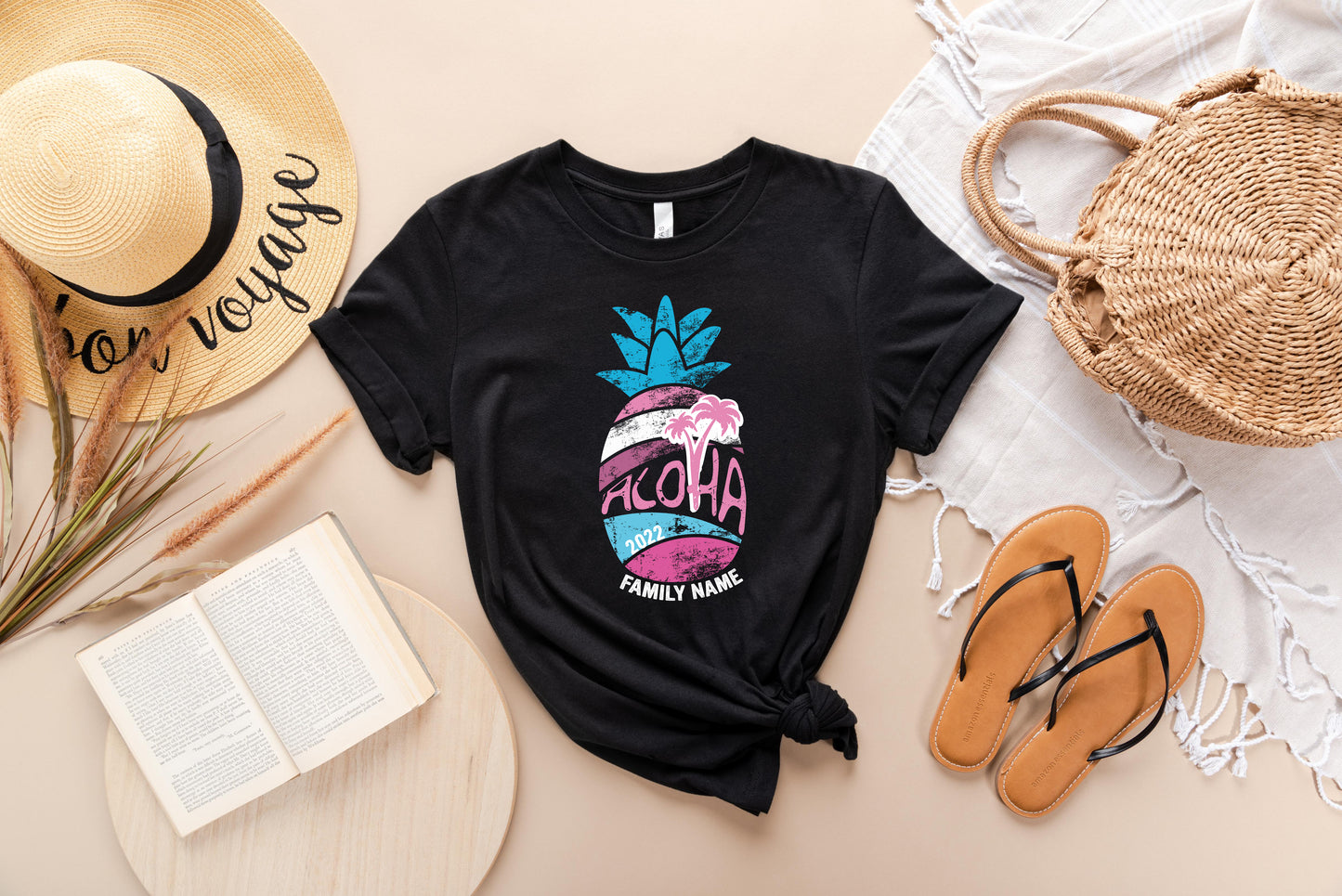 a casual outfit consisting of a black t-shirt with a pineapple graphic, a straw hat, a book, a pair of sandals, and a woven basket.