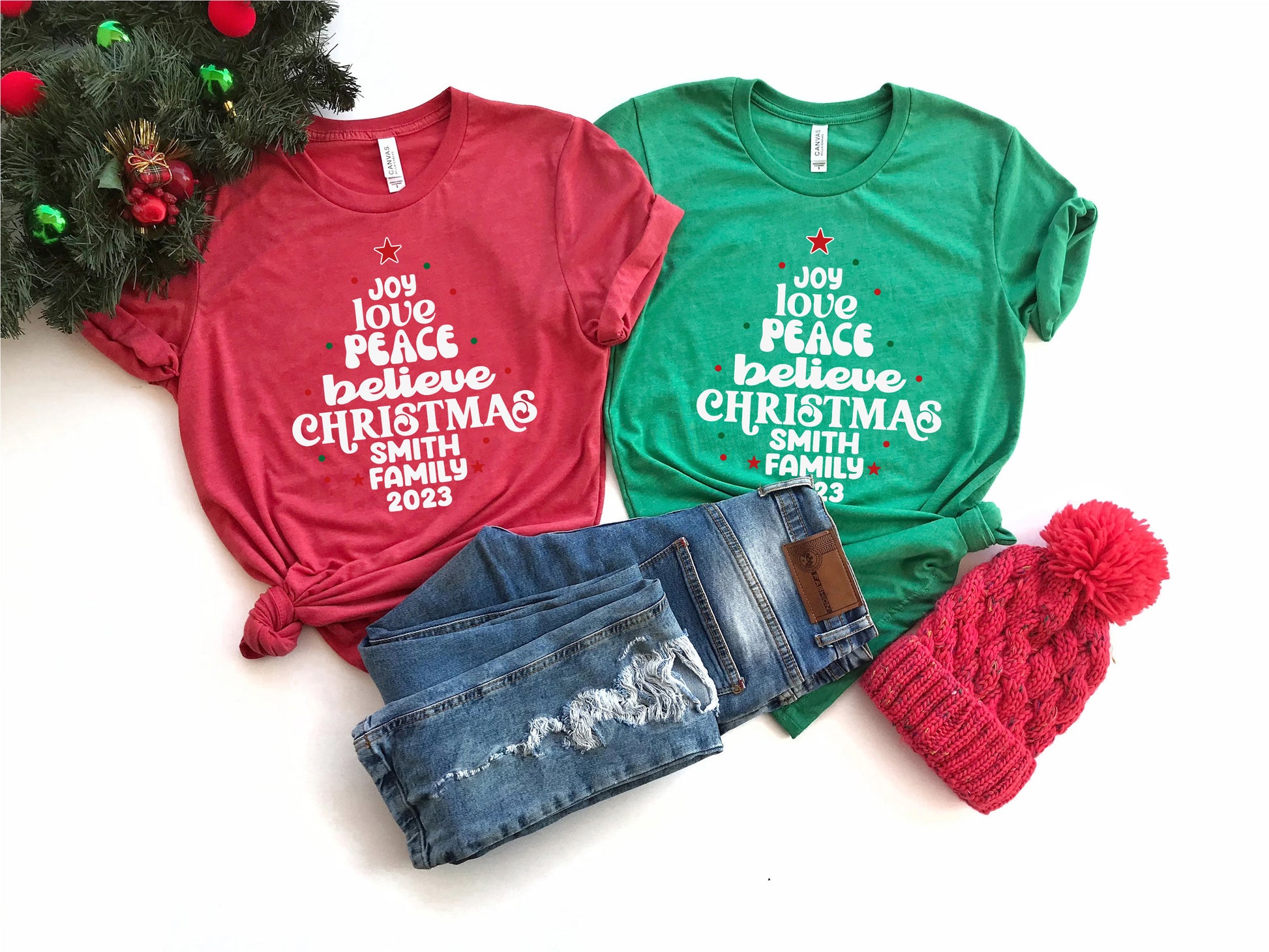 a collection of Christmas-themed items, including two t-shirts with holiday-themed text, a pair of jeans, and a red knit hat.