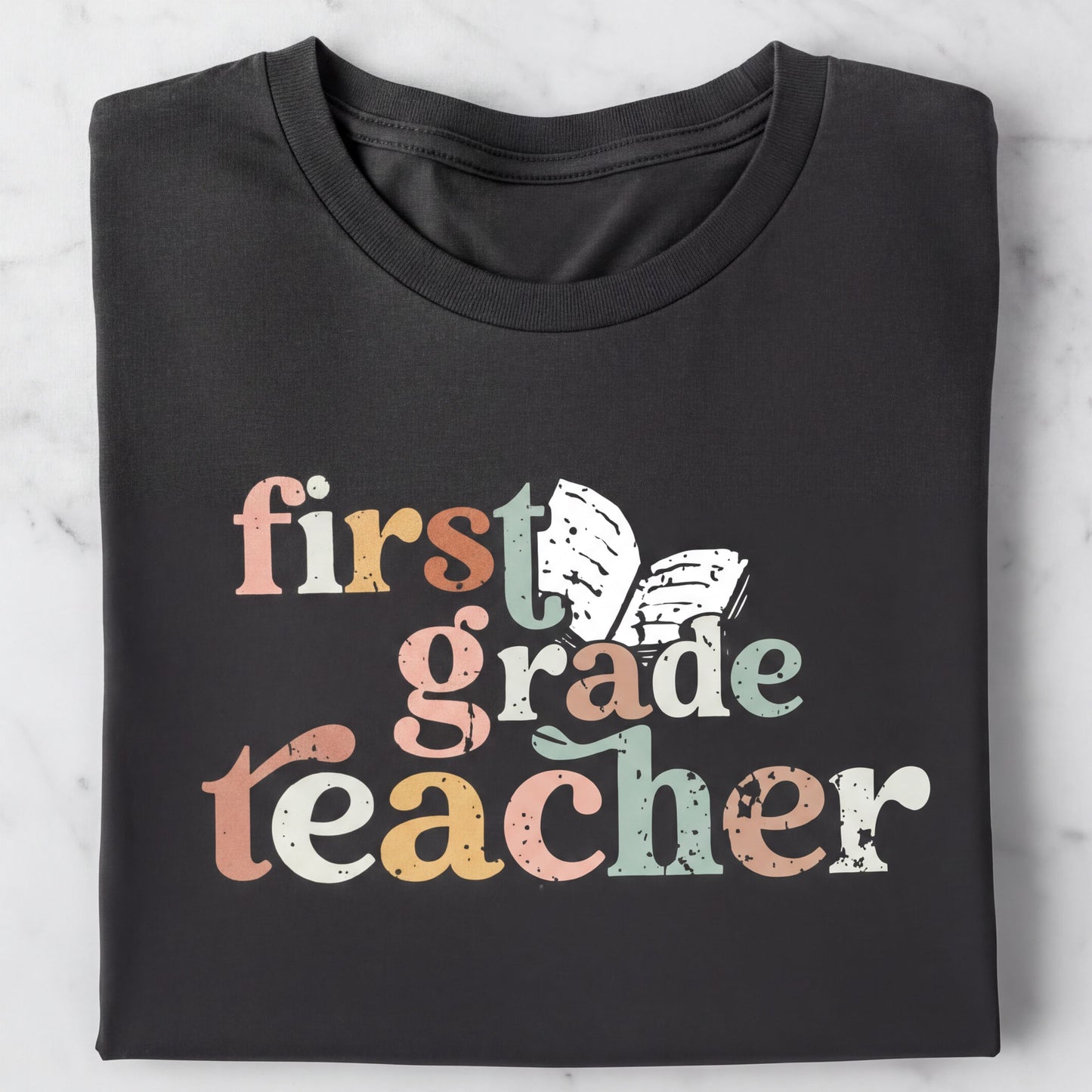 A black t-shirt with the text "first grade teacher" printed on it in a colorful, distressed font.