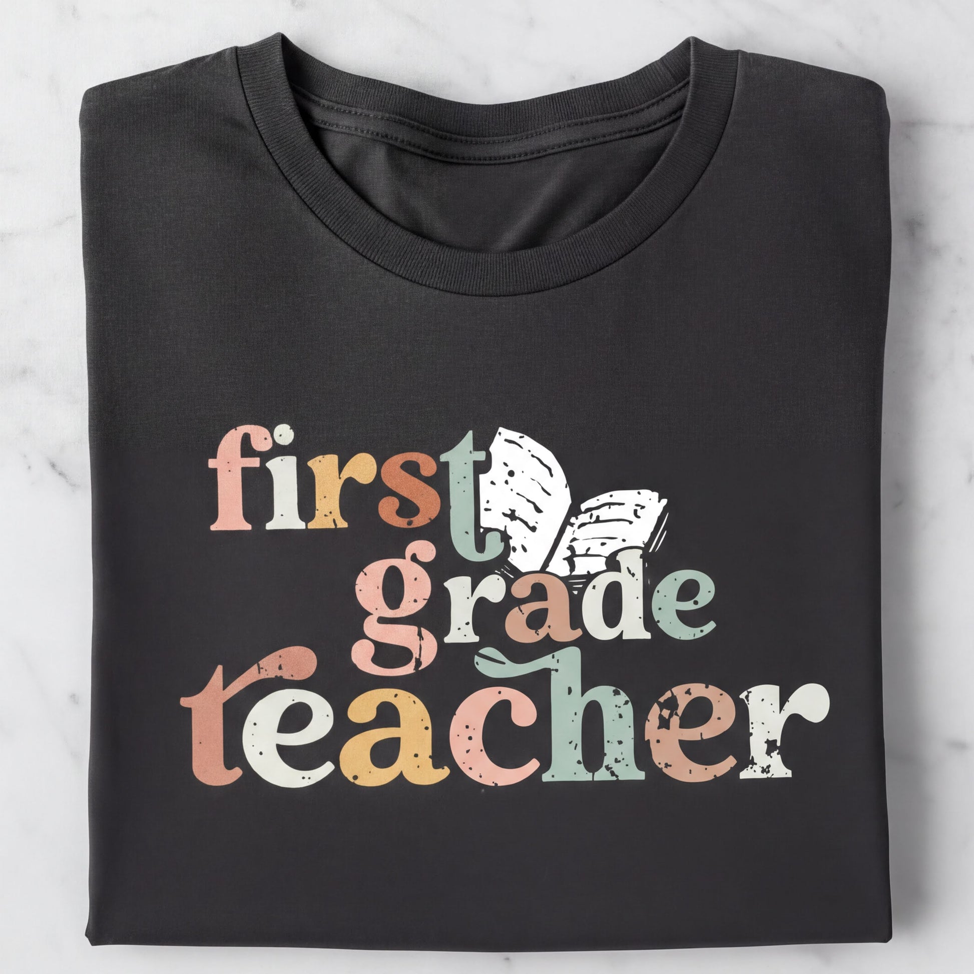 A black t-shirt with the text "first grade teacher" printed on it in a colorful, distressed font.