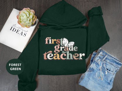 a green hoodie with the text "first grade teacher" printed on it, along with a pair of jeans and a book titled "Brilliant Ideas".