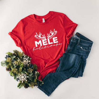 A red t-shirt with the text "MELE KOLIKINAS" printed on it, along with a pair of blue jeans and a wreath of pine cones.