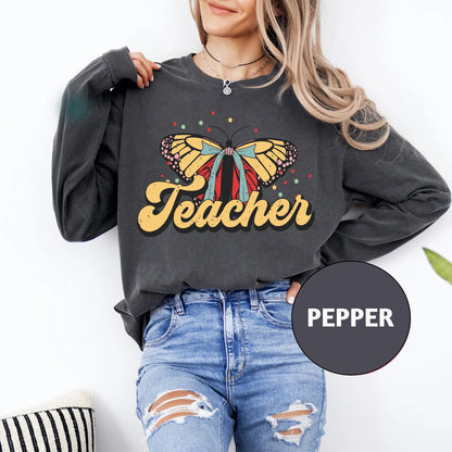 a woman wearing a sweatshirt that says teacher with a butterfly on it