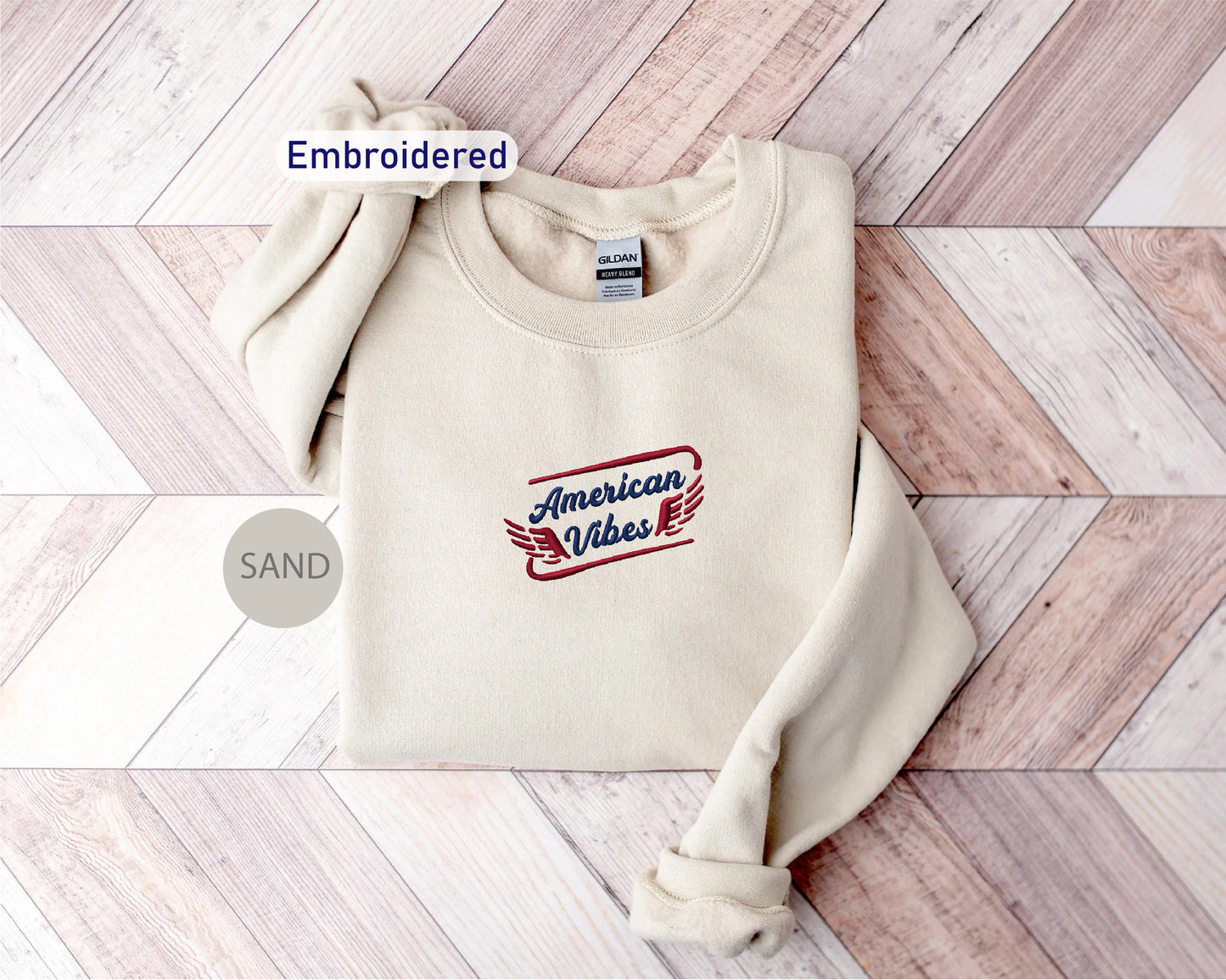 a cream-colored sweater with a red and blue embroidered design on the front, placed on a wooden surface.