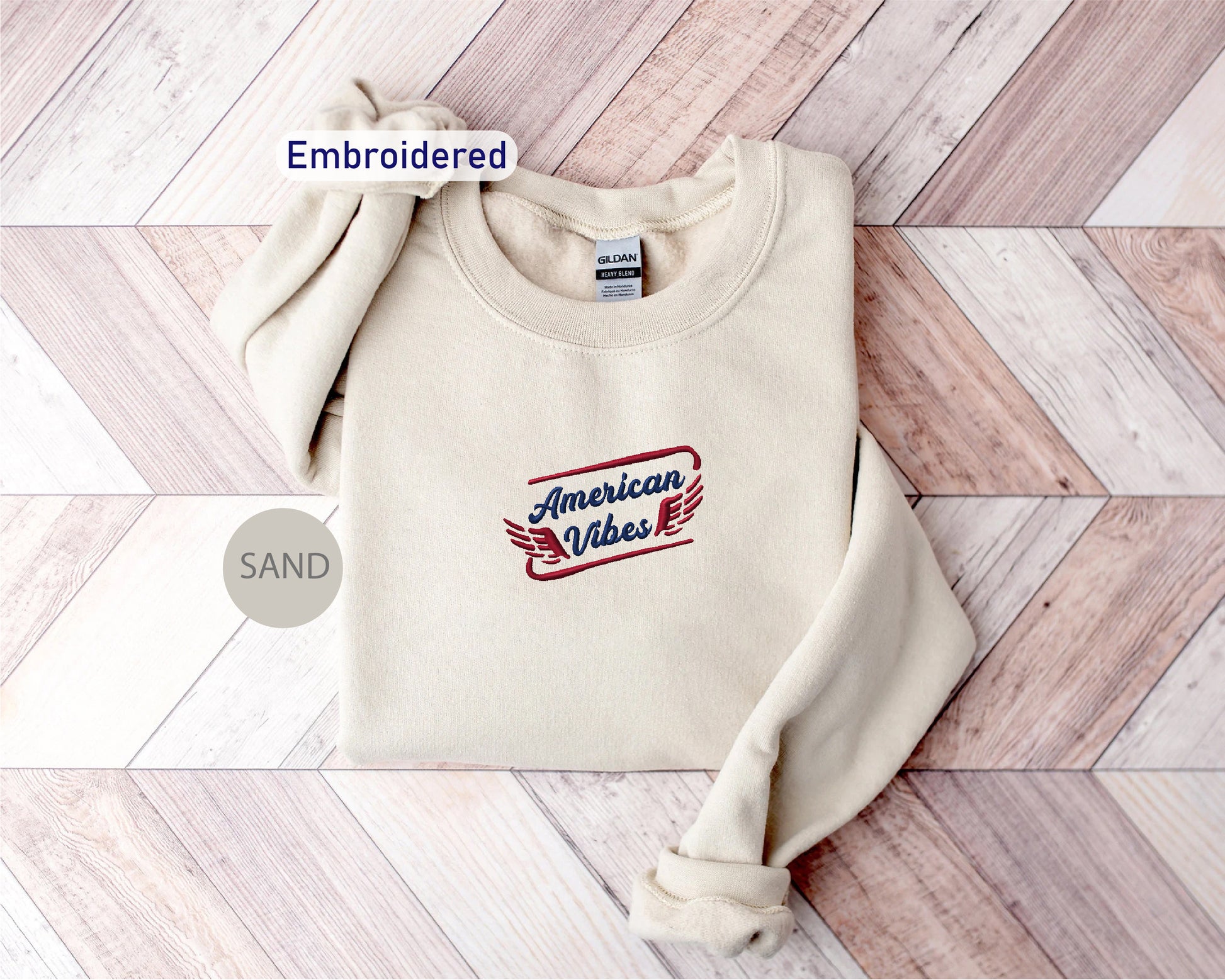 a cream-colored sweater with a red and blue embroidered design on the front, placed on a wooden surface.