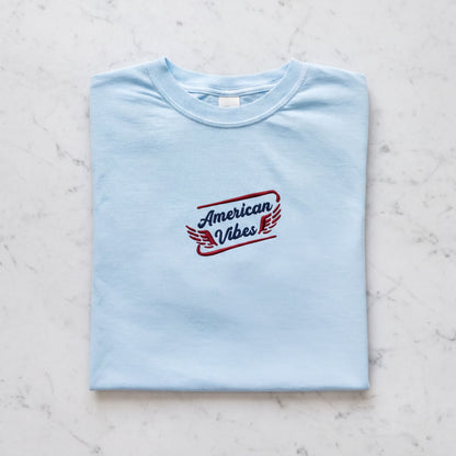A light blue t-shirt with the text "American Vibes" printed on it.