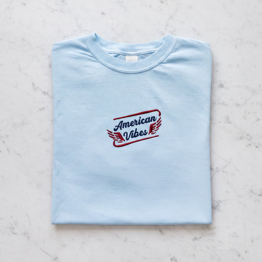 A light blue t-shirt with the text "American Vibes" printed on it.