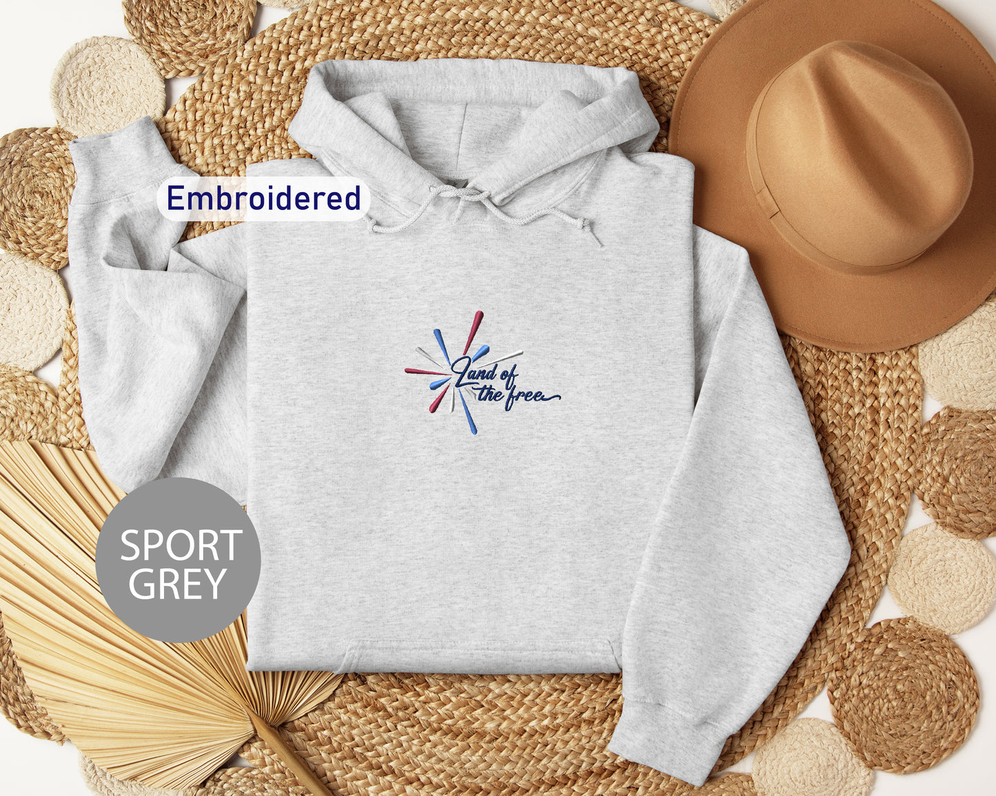 a grey hoodie with a colorful design, a brown hat, and some woven straw items, all arranged on a woven mat.
