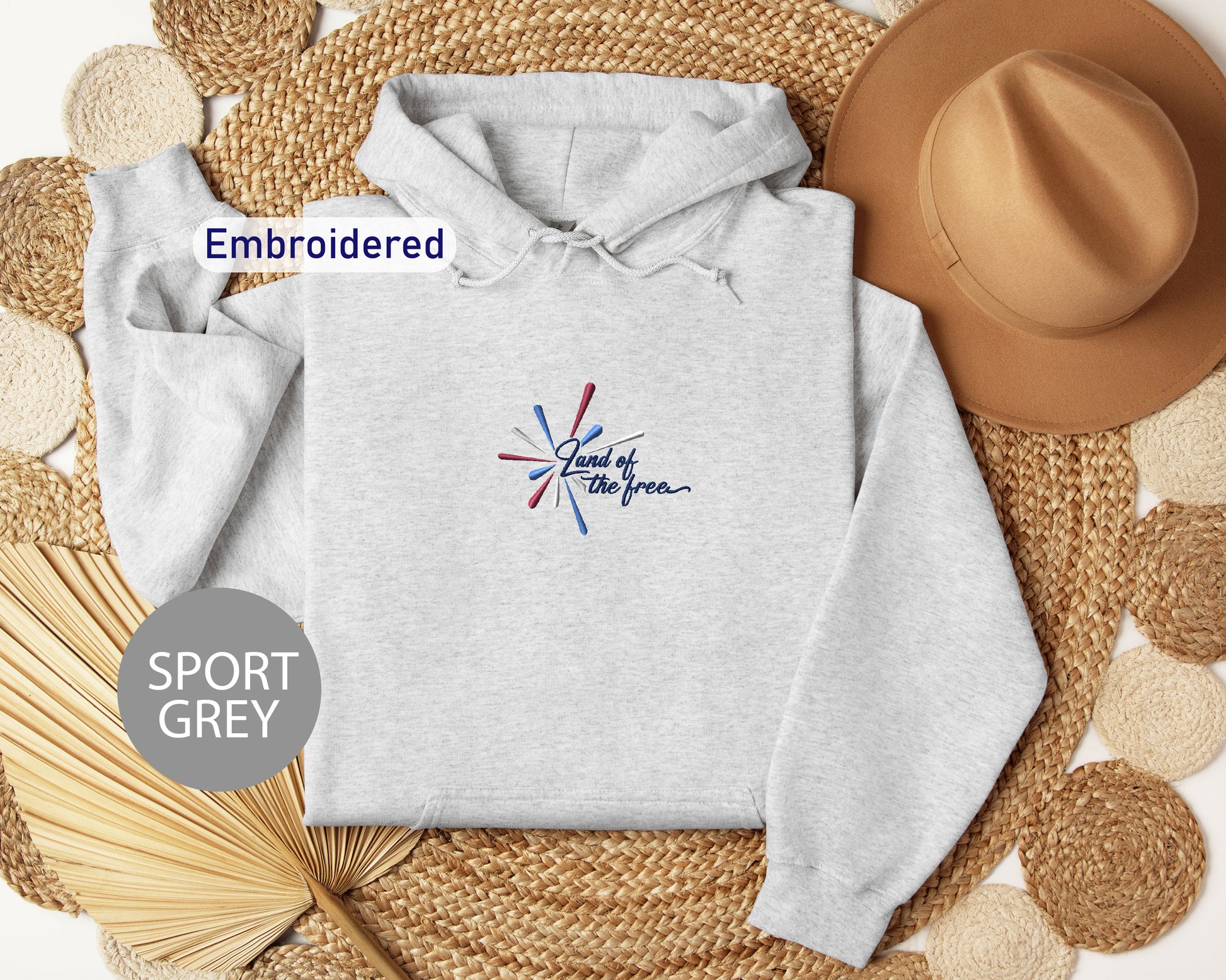 a grey hoodie with a colorful design, a brown hat, and some woven straw items, all arranged on a woven mat.